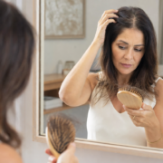 cabelo-caindo-muito-slimcenter.webp Mulher percebendo aumento da queda de cabelo enquanto observa os fios em ambiente natural.