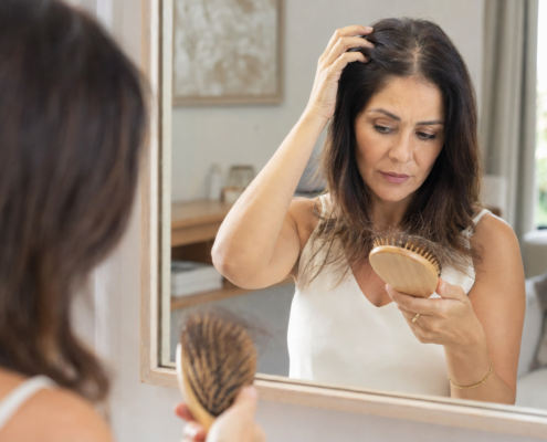 Mulher percebendo aumento da queda de cabelo enquanto observa os fios em ambiente natural.